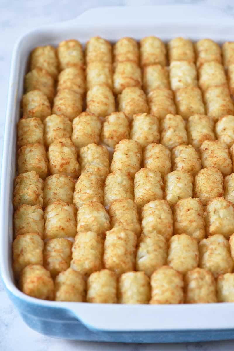 topping tater tot casserole with tater tots in blue and white baking dish