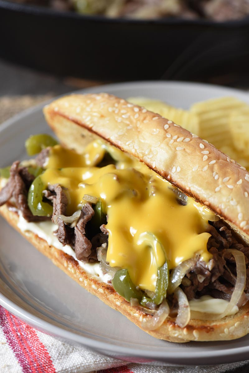 Philly cheesesteak sandwich with Cheez Whiz on gray plate with potato chips