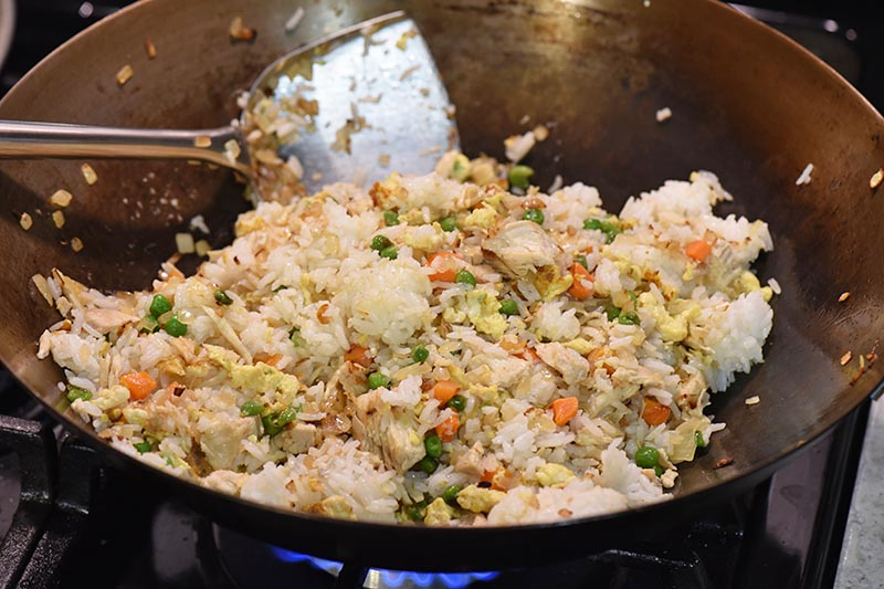 stir frying rice into chicken fried rice wok recipe in large wok with wok spatula