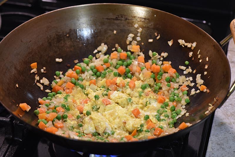 scrambling eggs with vegetables in large wok for chicken fried rice recipe