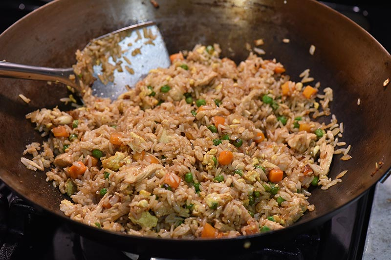 stirring chicken fried rice together with soy sauce in large wok with large wok spatula