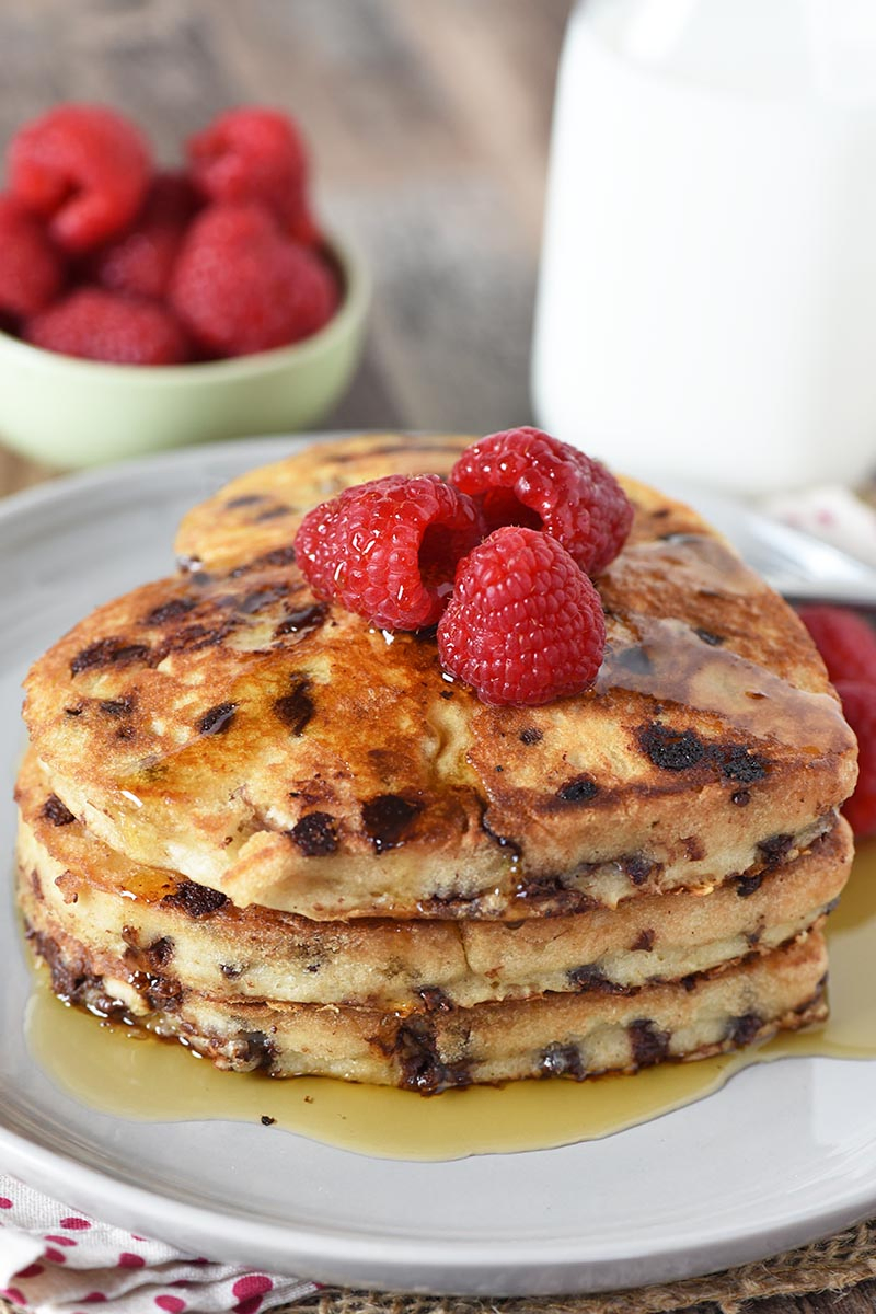 stack of heart pancakes on gray plate, topped with raspberries and maple syrup