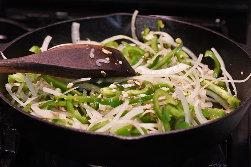 cooking vegetables for cheese steak recipe in cast iron skillet with wooden spatula