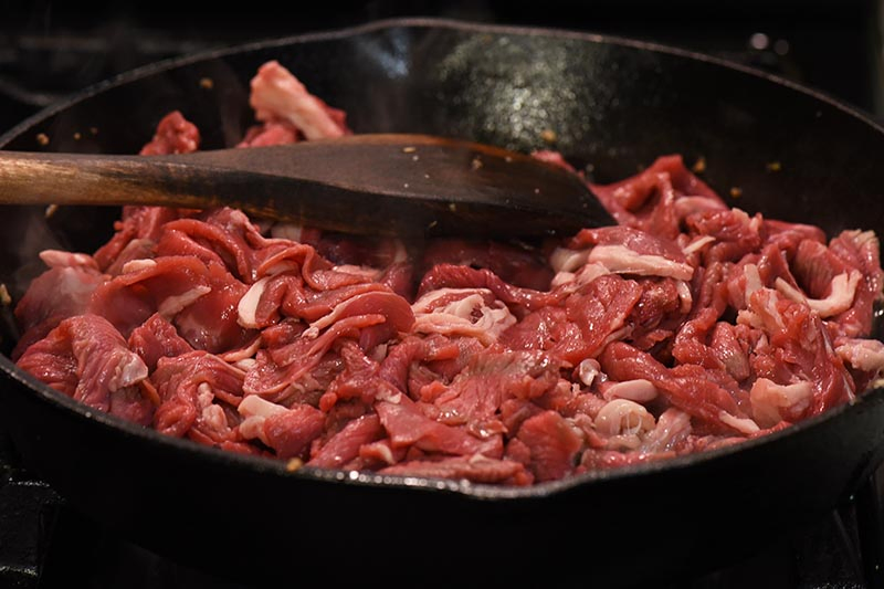 cooking thinly sliced sirloin steak for Philly cheese steak meat in cast iron skillet