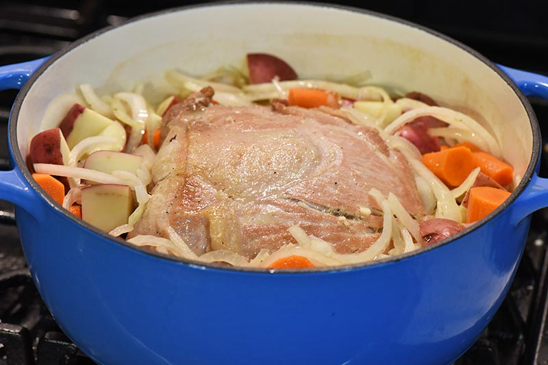 cooking pork roast with vegetables in blue Dutch oven