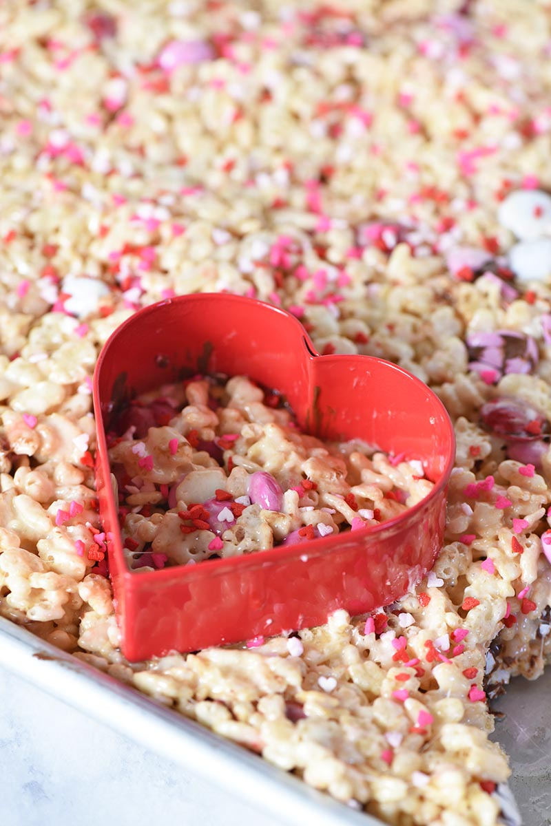 cutting heart shaped Rice Krispie treats with red heart shaped cookie cutter in brownie pan