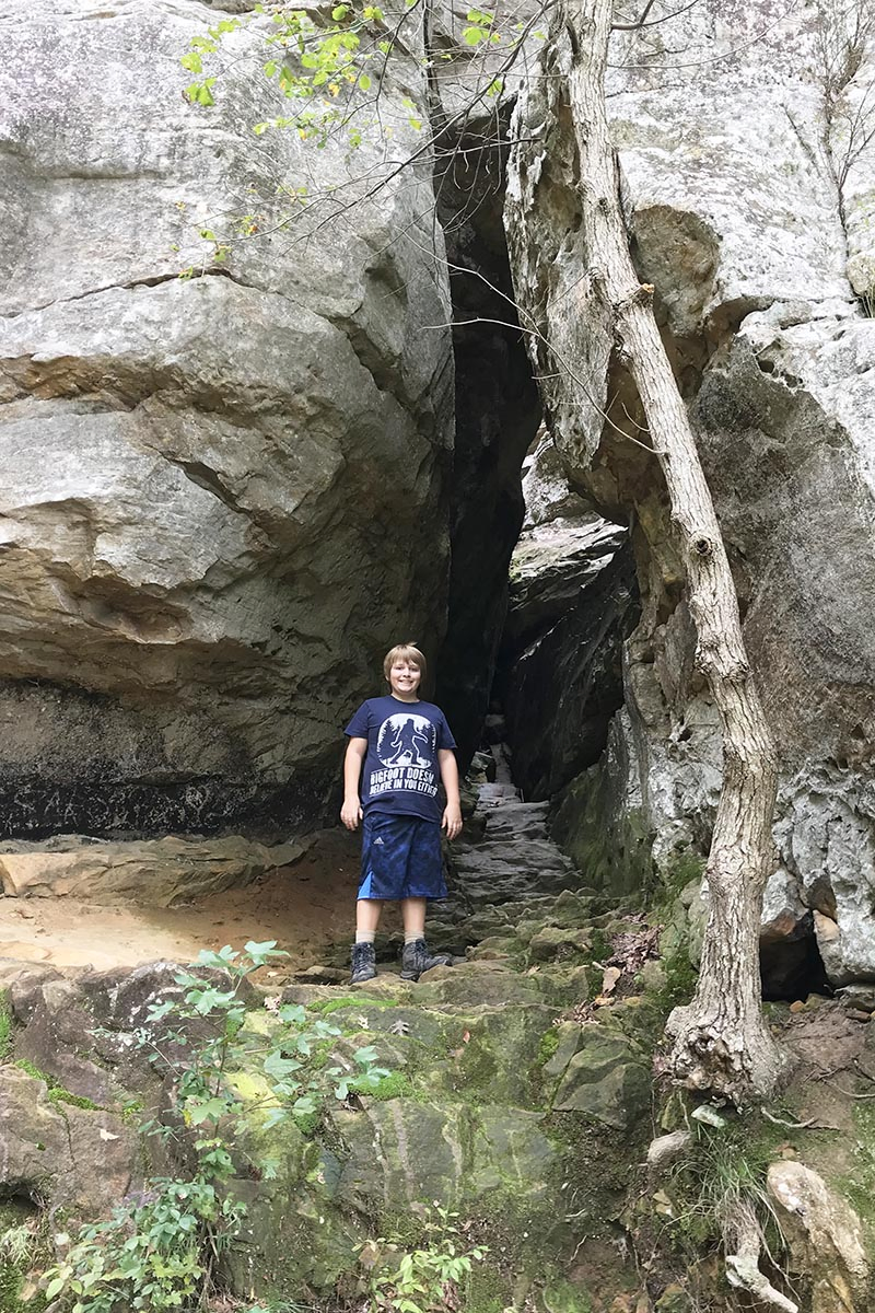 boy with Bigfoot shirt exploring crevice along Bear Cave Trail in Petit Jean State Park