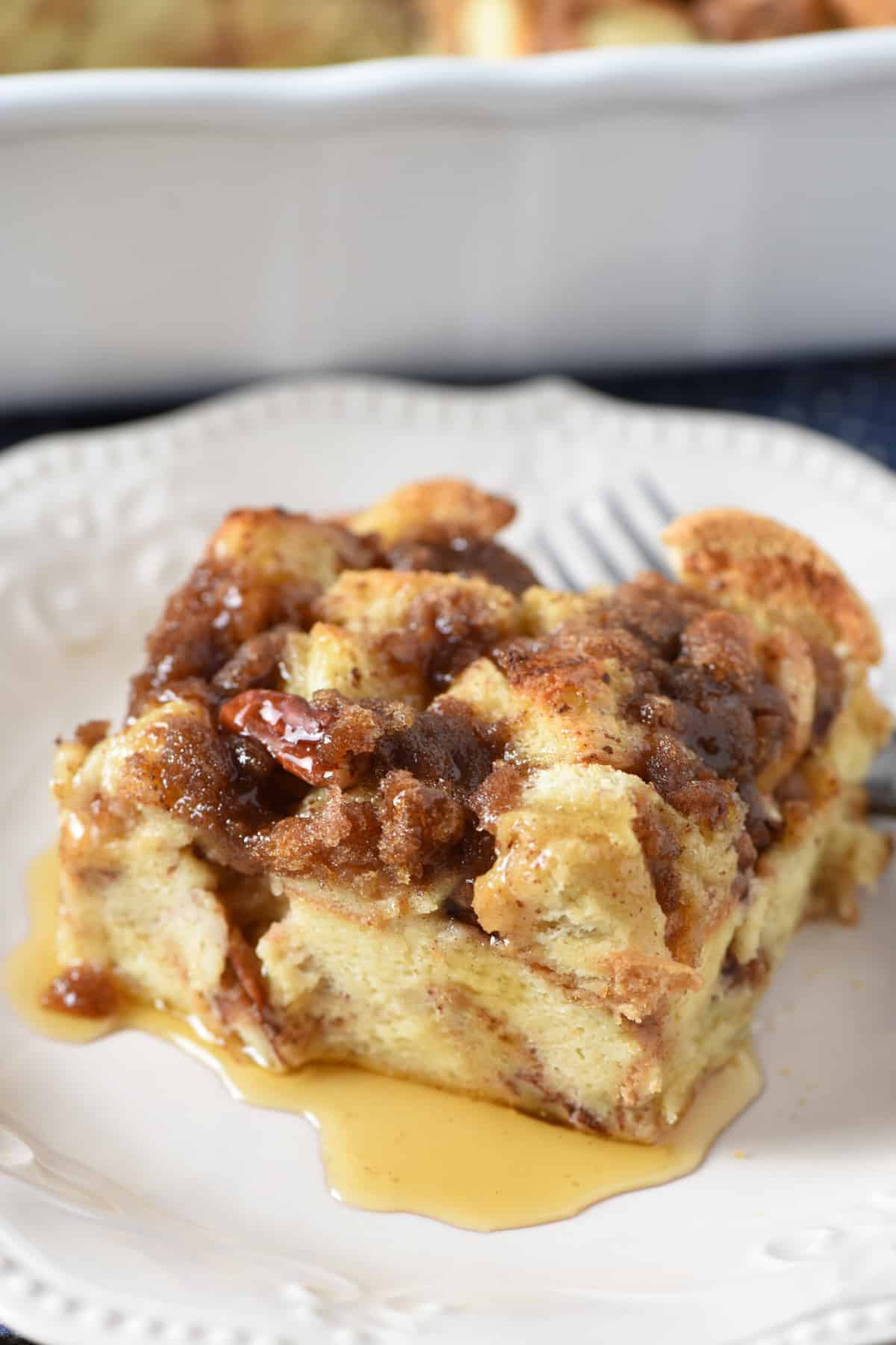 slice of French toast casserole on white plate with maple syrup and fork