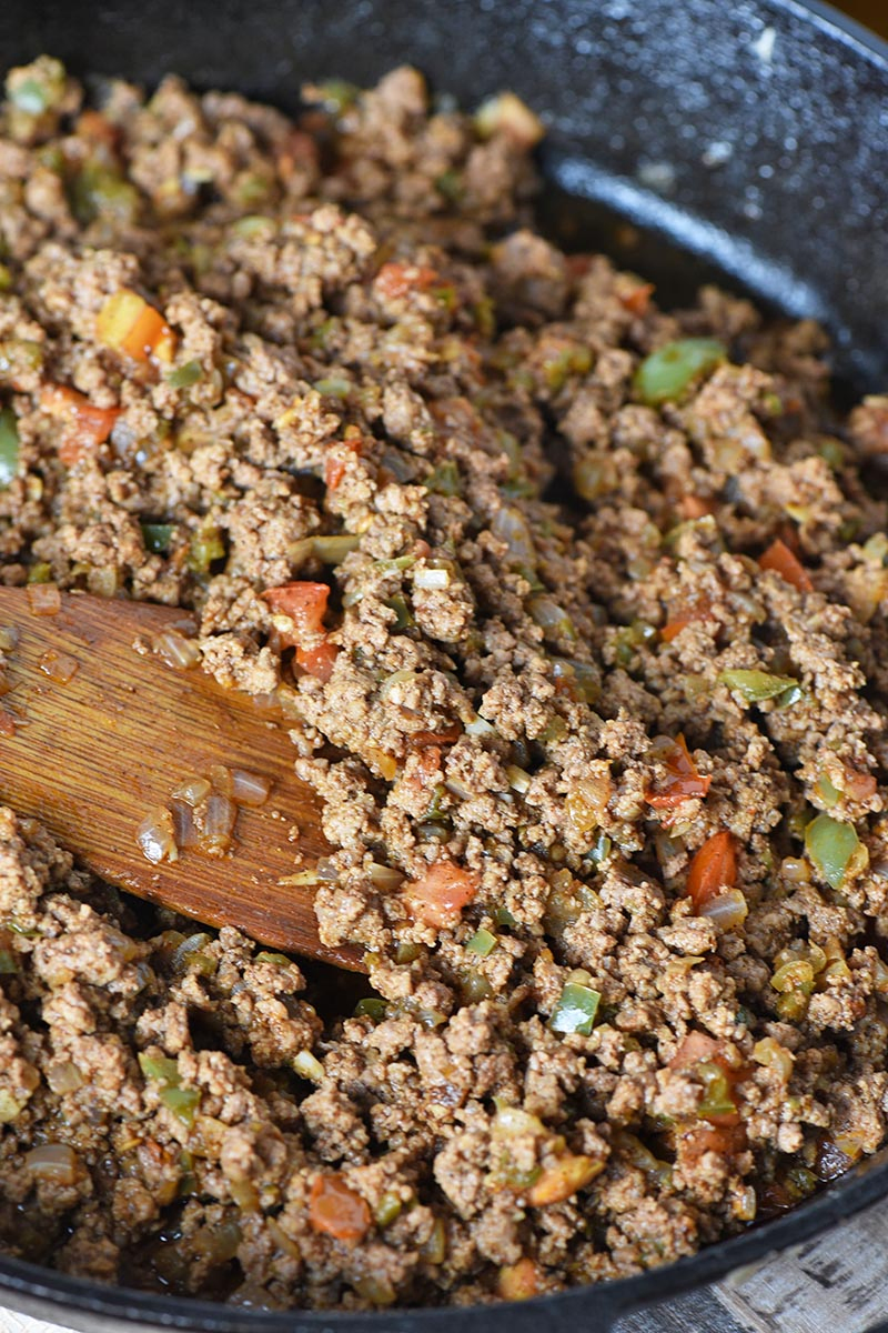 ground beef taco meat for easy stuffed peppers, Mexican style, in cast iron skillet with wooden spatula