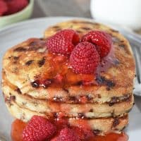 heart shaped chocolate chip pancakes stacked on gray plate, slathered with raspberries and strawberry jam