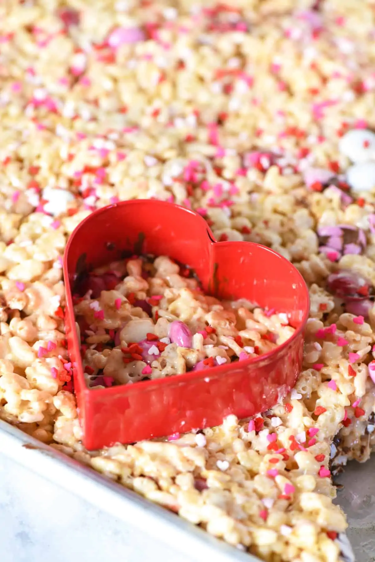 cutting heart shaped Rice Krispie treats with red heart cookie cutter