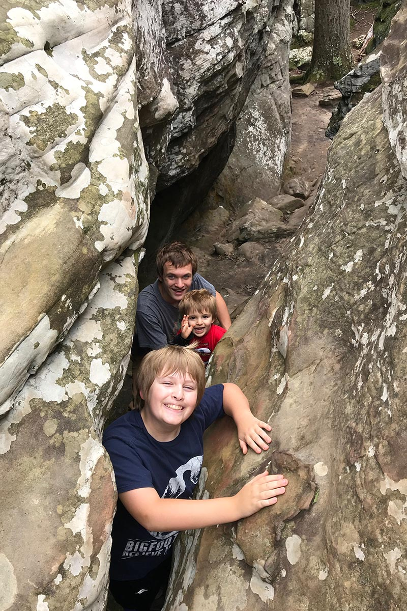 boys exploring a crevice between boulders and rocks on Bear Cave Trail in Petit Jean State Park