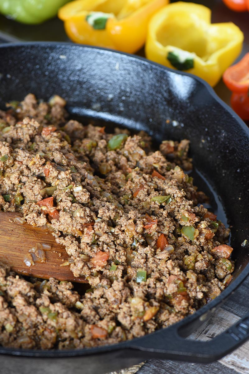 ground beef taco meat in cast iron skillet and prepared bell peppers for taco stuffed pepper recipe