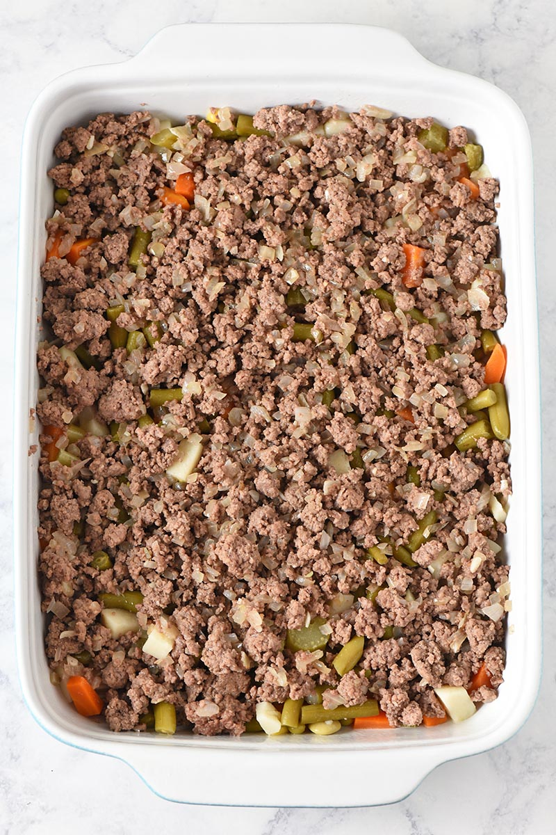layering browned ground beef in blue and white casserole dish for tater tot casserole recipe