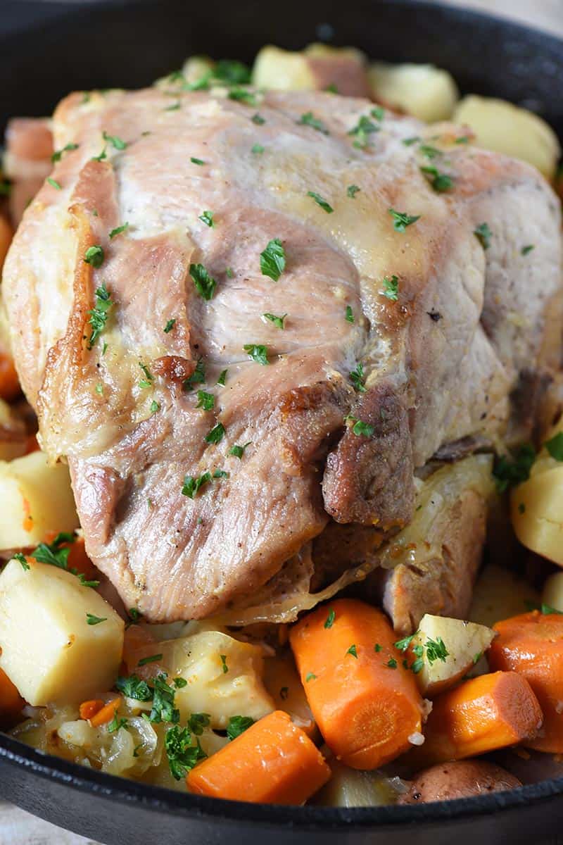 pork roast recipe, oven roasted with potatoes, carrots, and onions in cast iron pan, with parsley sprinkled on top