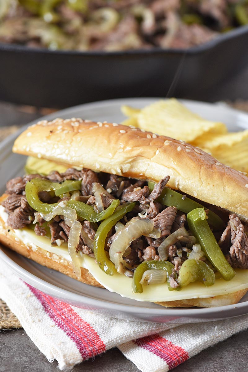 Philly cheesesteak sandwich with provolone cheese, served on gray plate with potato chips