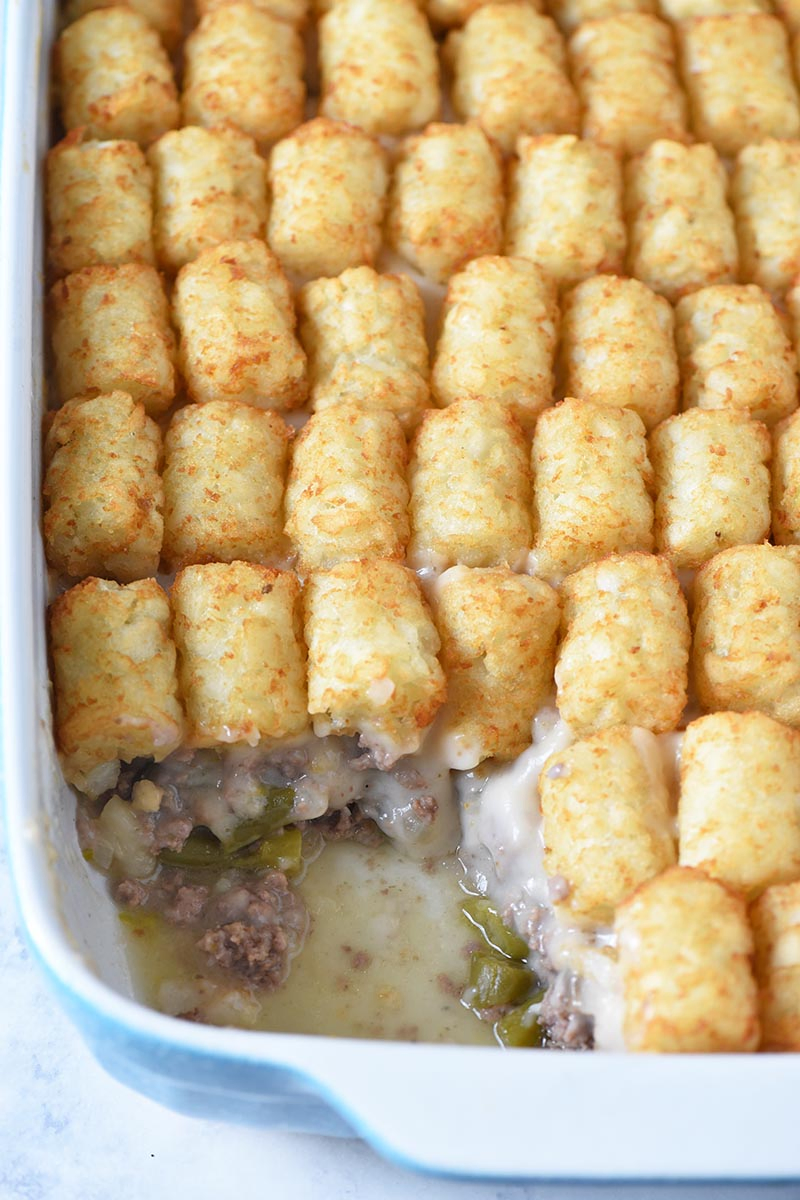 scooping tater tot hotdish out of blue casserole dish