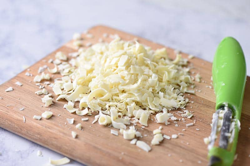 shredding white chocolate with a vegetable peeler on a wooden cutting board