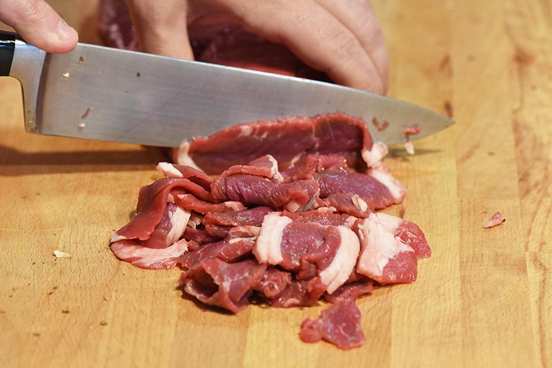 hands slicing Philly cheese steak meat on cutting board with knife