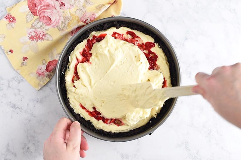 adding second half of raspberry cheesecake batter to springform baking pan with a spatula