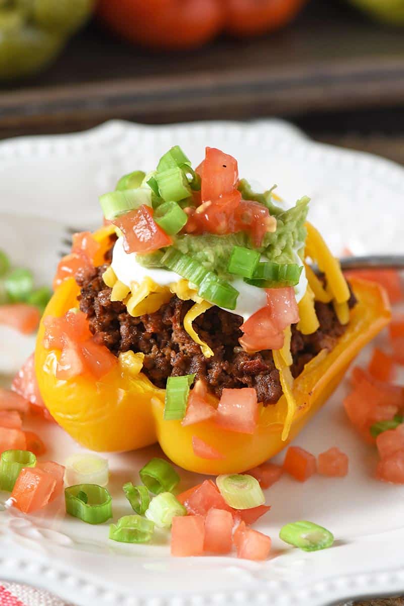 yellow taco stuffed pepper on white plate with taco toppings