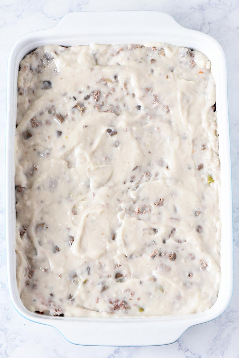 layering cream of mushroom soup onto ground beef in tater tot casserole, in blue and white casserole dish