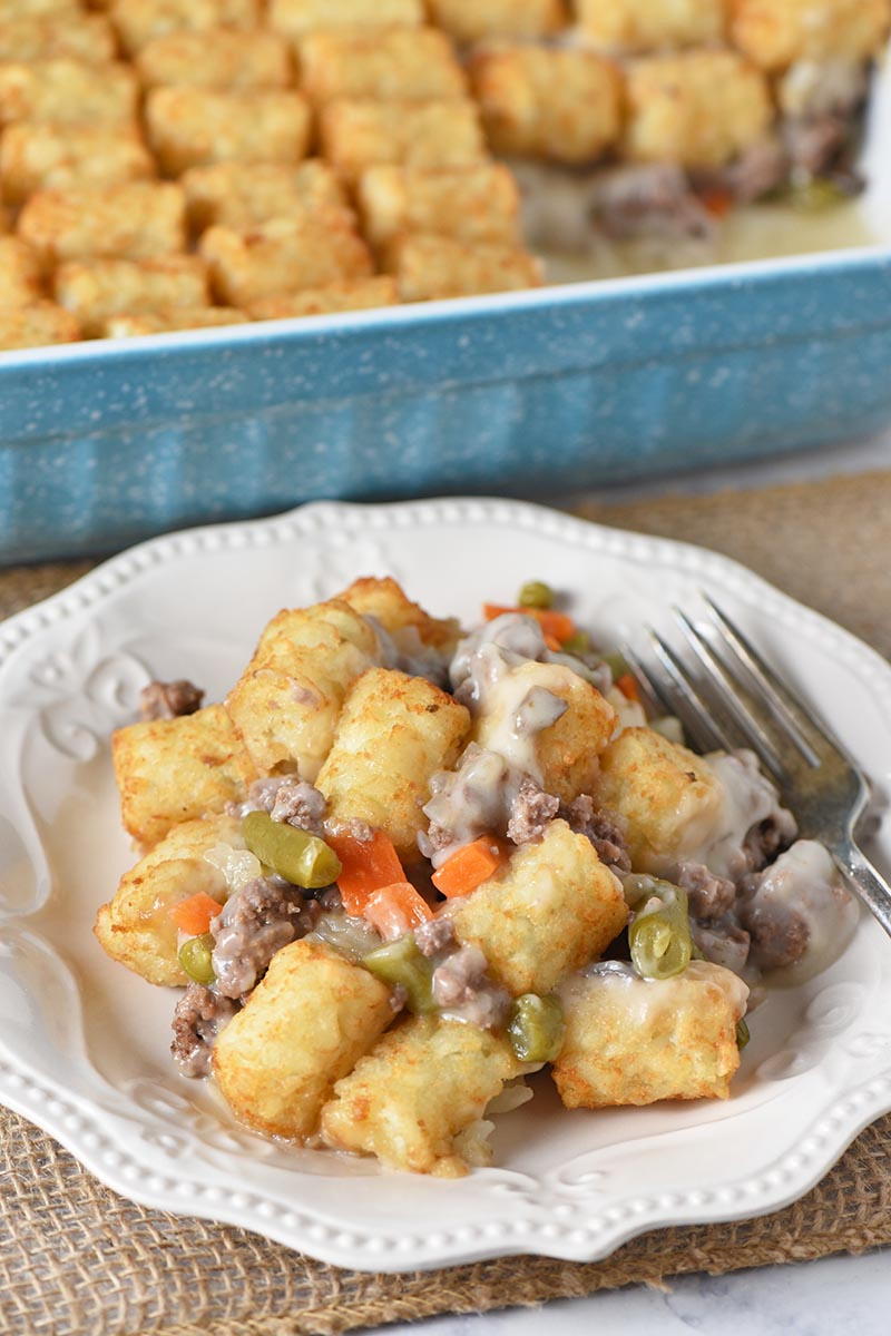 tater tot casserole with veggies served on white plate with blue casserole dish