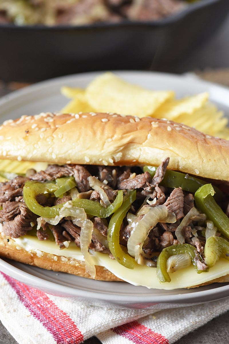 close up look at a traditional Philly cheese steak on a gray plate with potato chips