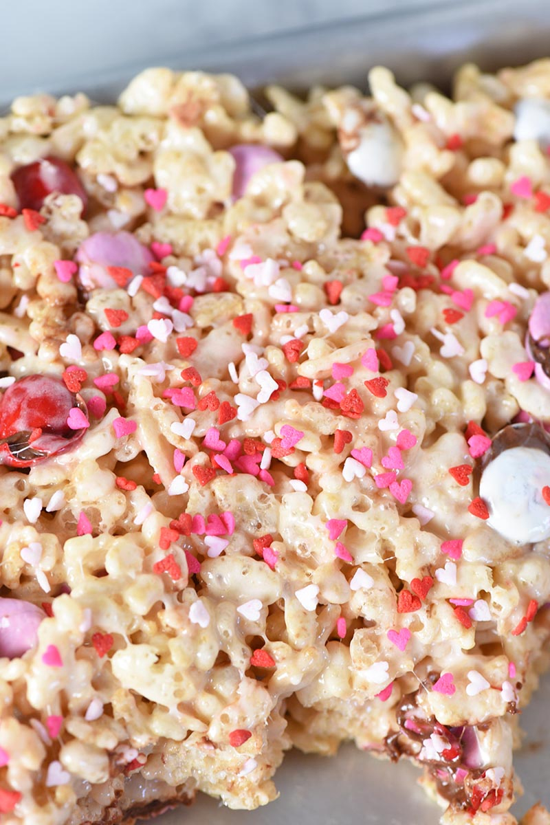 adding heart shaped Valentine sprinkles to Rice Krispie treats, making Valentine's Day treats