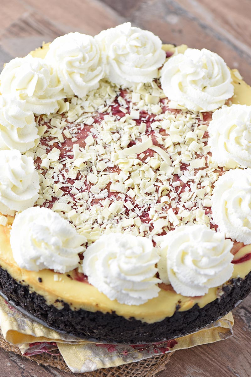 whole white chocolate raspberry cheesecake with white chocolate flakes and swirls of whipped cream on top
