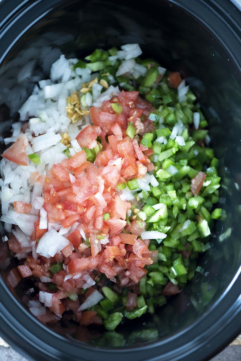 chopped and minced onion, garlic, tomatoes, and bell peppers in slow cooker crock for chicken enchilada soup recipe