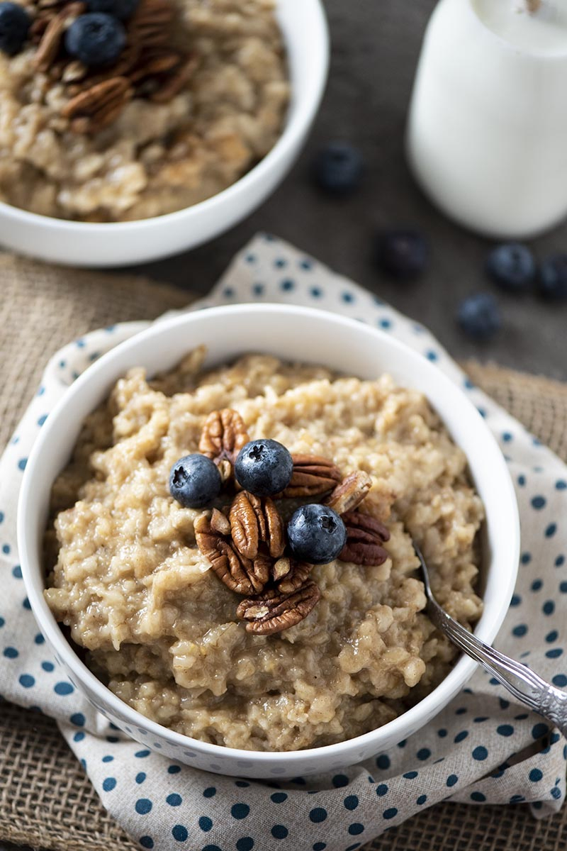maple oats in white bowl with spoon, pecans, and blueberries