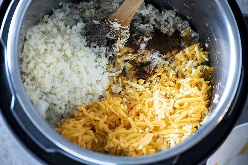 adding shredded cheese, cauliflower, and spices to low carb chicken casserole in Instant Pot pressure cooker