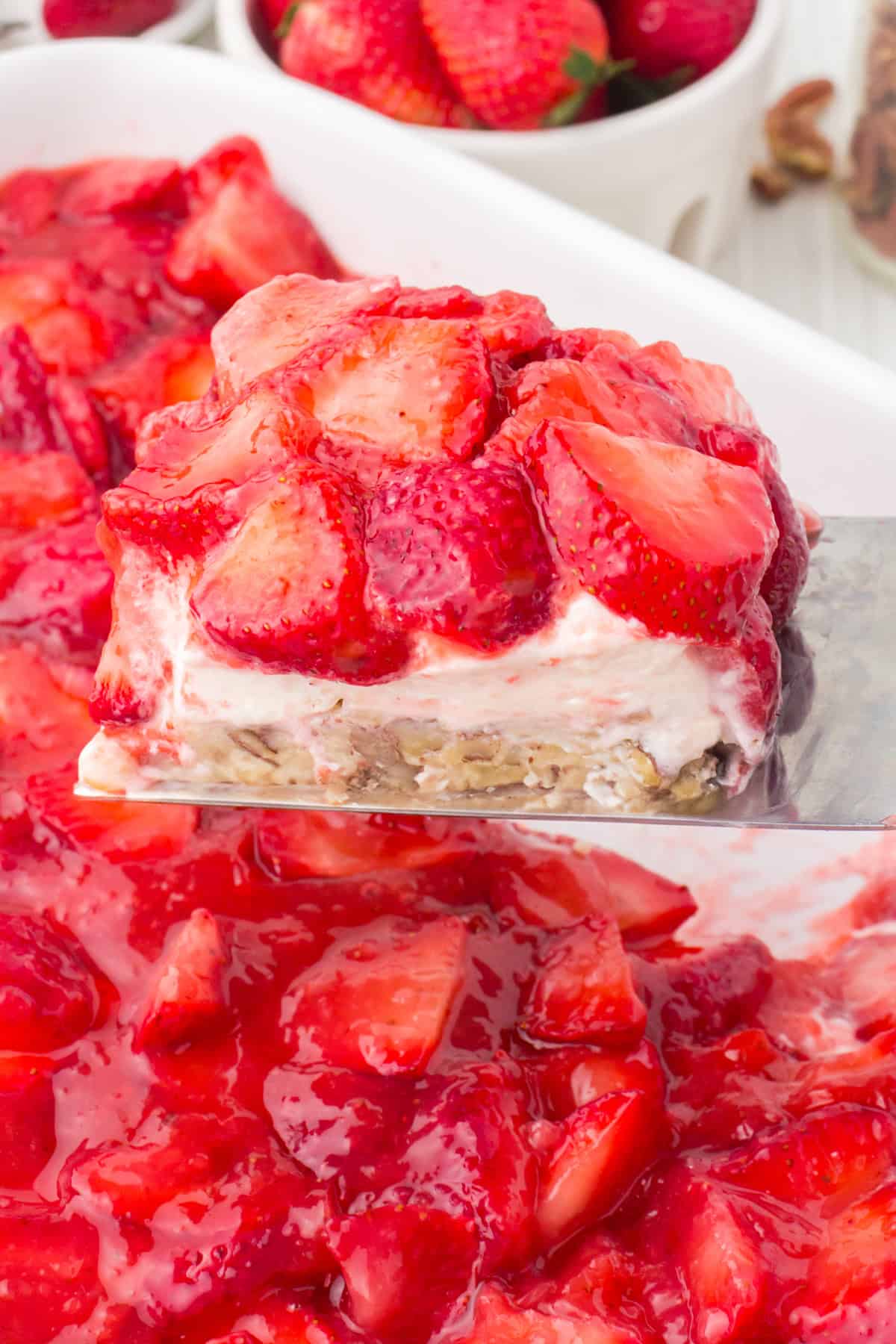 silver spatula holding up a slice of strawberry delight over a white 13x9 casserole dish