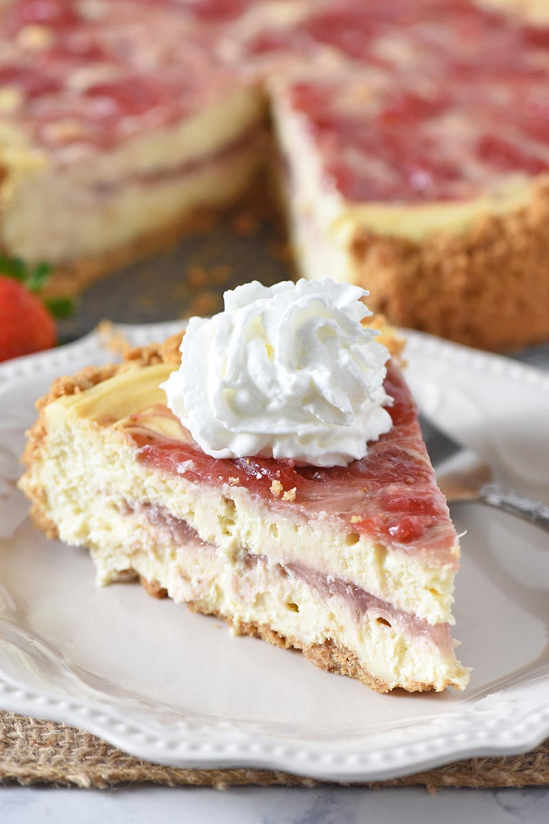 slice of strawberry swirl cheesecake on white plate with whipped cream and a fork