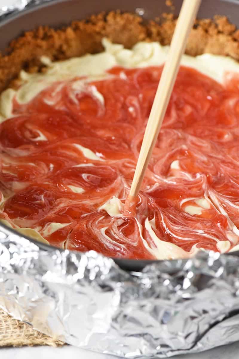 swirling strawberry sauce for cheesecake into strawberry swirl cheesecake filling with wooden skewer