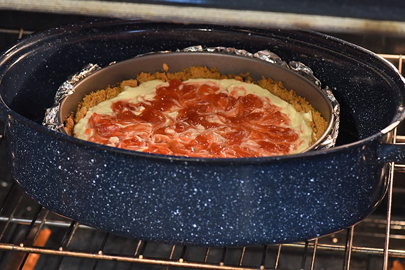 baking strawberry swirl cheesecake in roasting pan with water in oven