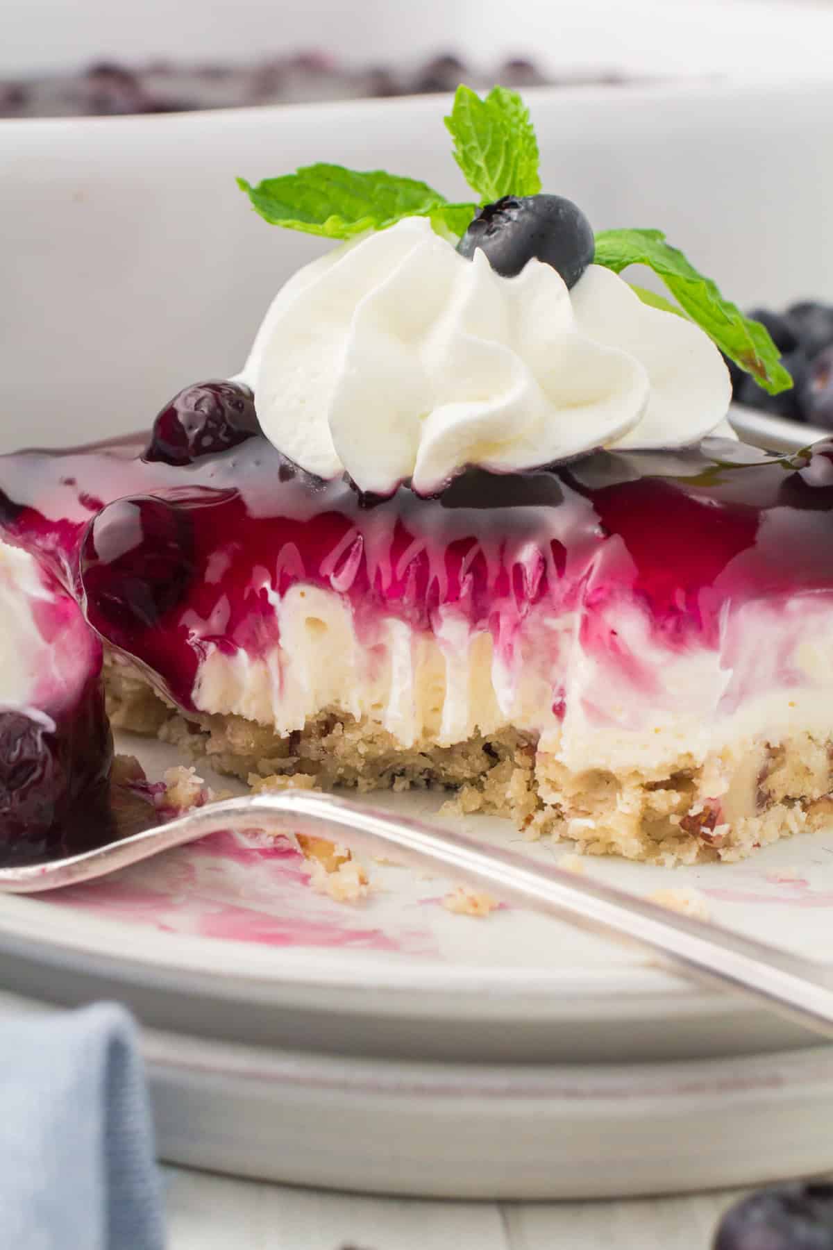 closeup photo showing a slice of blueberry yum yum dessert on a small gray plate with a dollop of whipped cream and fresh blueberries on top
