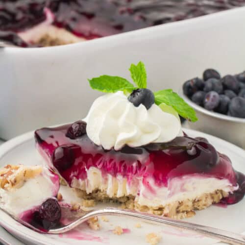 slice of no bake blueberry yum yum on a small white plate with a dollop of whipped cream on top