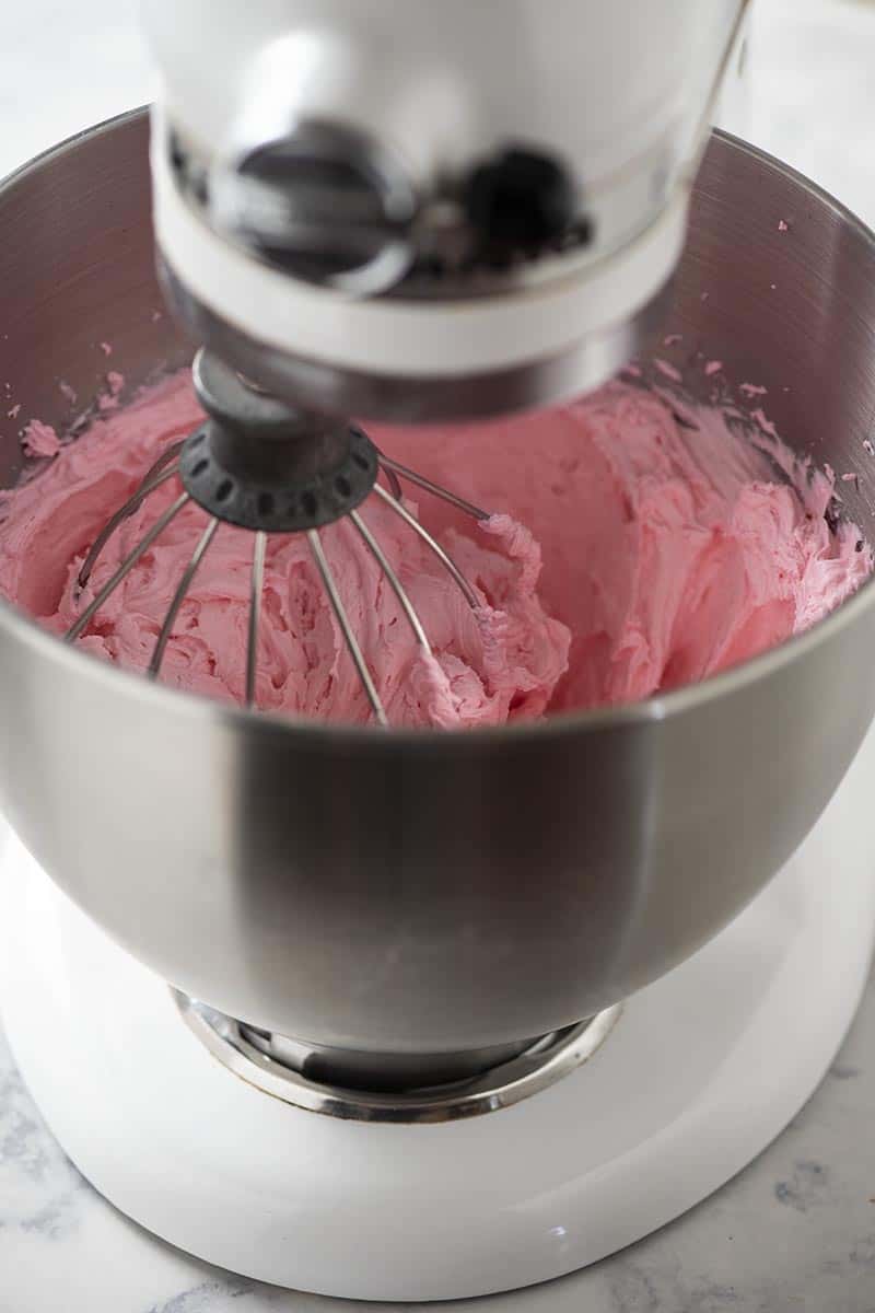 white KitchenAid mixer with pink buttercream frosting in mixing bowl