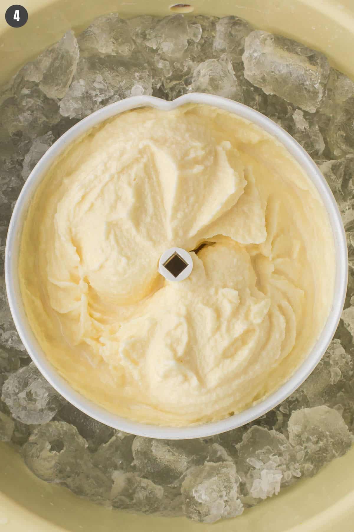 closeup shot showing old fashioned homemade ice cream in a metal ice cream maker canister that's set down inside of an ice cream maker tub full of crushed ice and rock salt