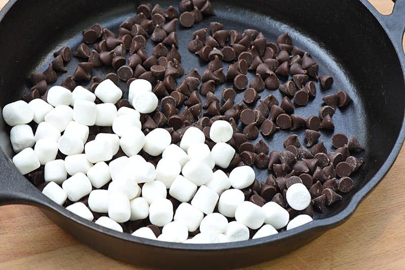 layer of chocolate chips and mini marshmallows for s'mores dip in cast iron skillet