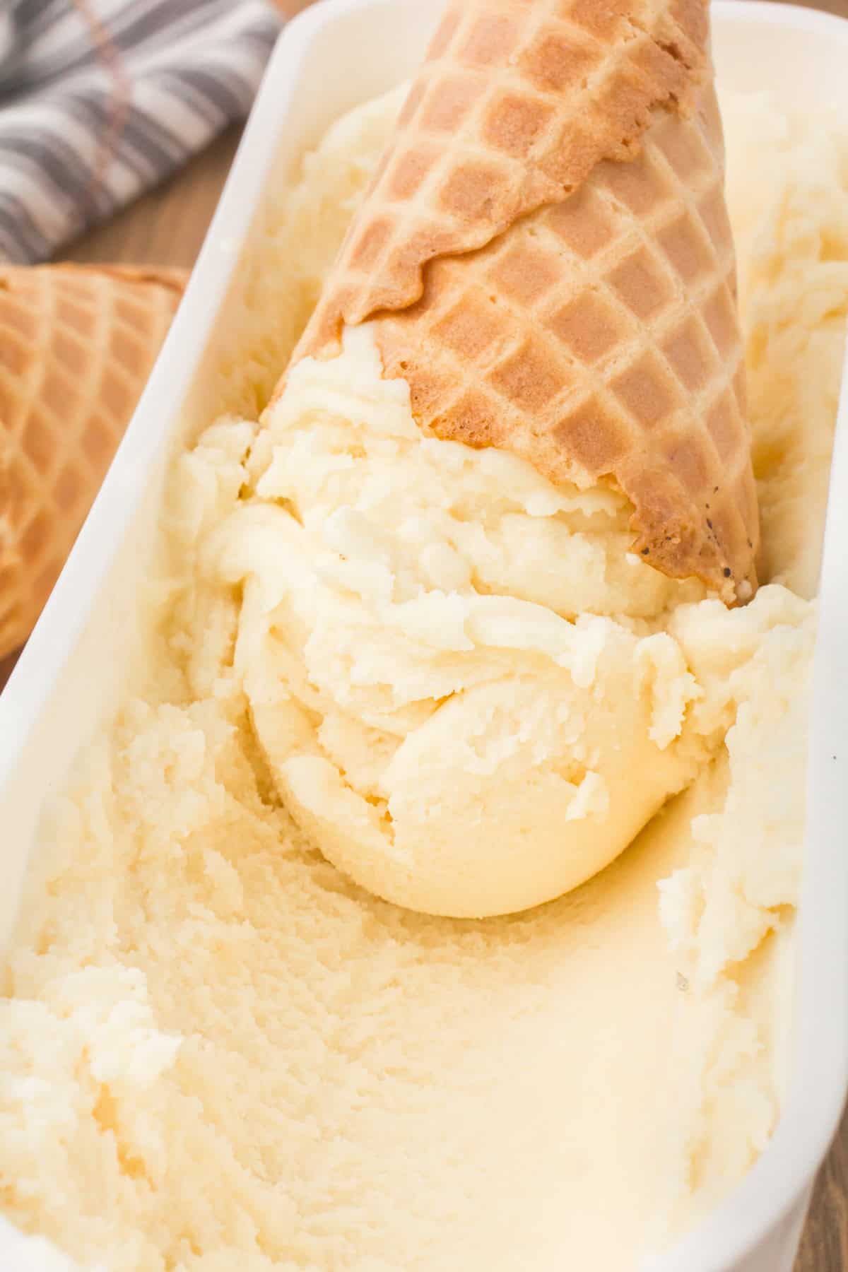closeup shot showing southern homemade ice cream in a waffle cone set inside of a tub full of old fashioned homemade vanilla ice cream
