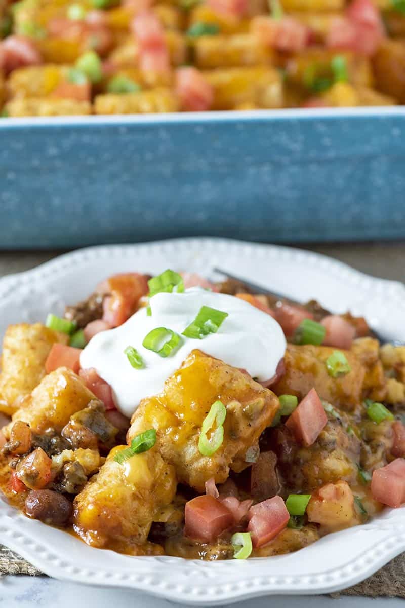 Mexican tater tot casserole topped with sour cream and green onions on white plate