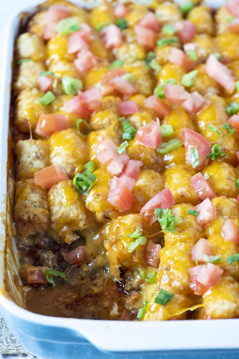 tater tot taco bake with scoop missing in blue baking dish