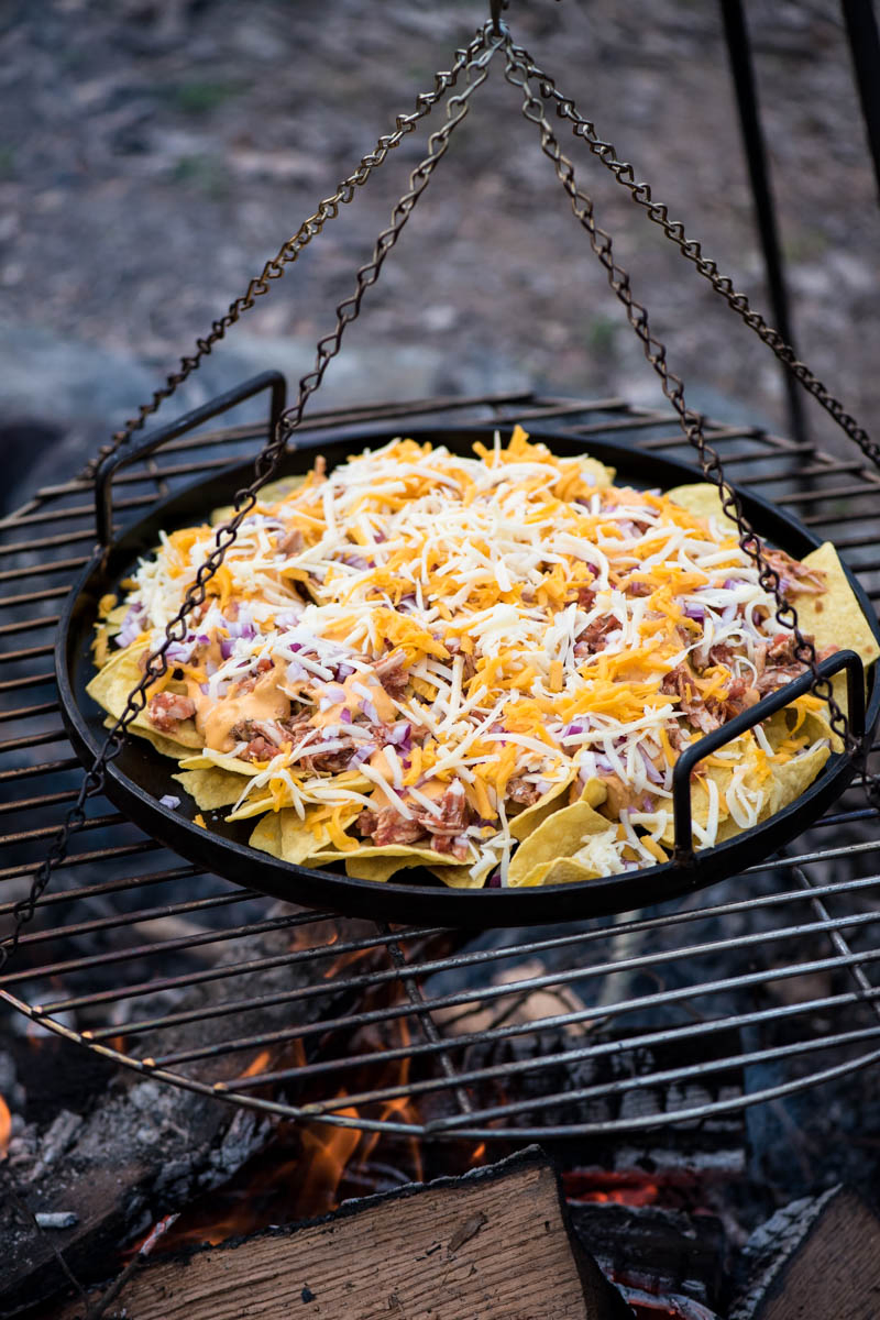cooking chicken nachos over the campfire on a large cast iron griddle