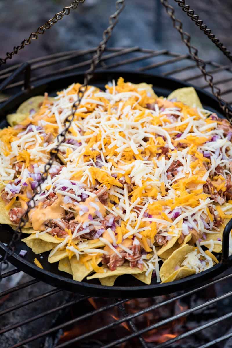 cooking chicken nachos on a cast iron pan over the campfire