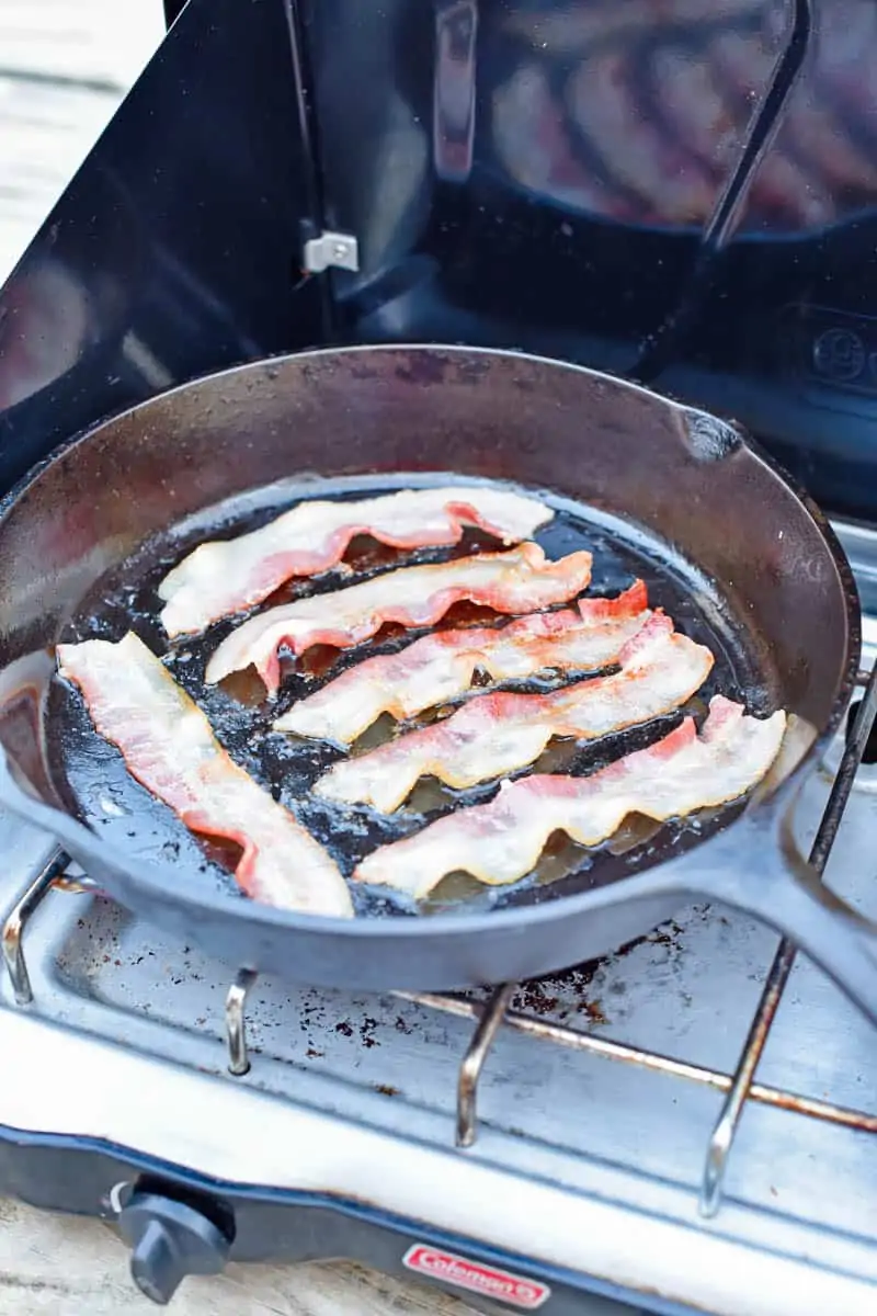 cooking bacon in a cast iron skillet on a camp stove