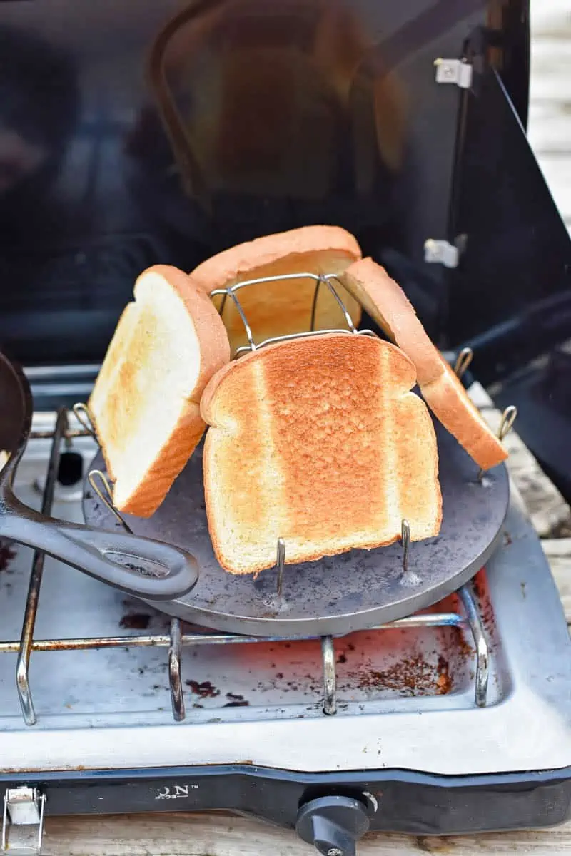 camping cooking equipment, including camp stove, cast iron skillet, and camp stove toaster with bread toasting