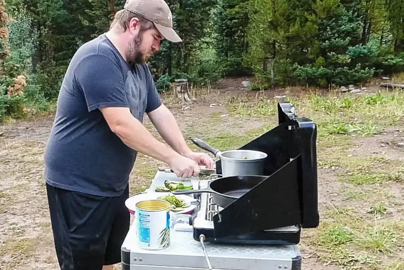 man cooking chicken fajitas outdoors on camp stove on camping kitchen table